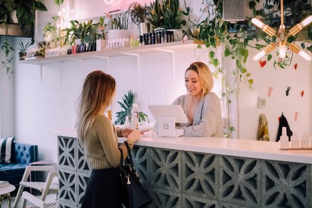 One woman is paying a fee with Easy Salon Software to another at the salon.